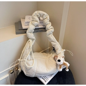 Detail of white quilted dumpling bag with cute plush puppy charm on a navy cushion
