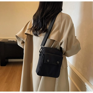 Dettaglio di una borsa a tracolla compatta in nylon nero su una modella in trench beige