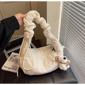 Detail of white quilted dumpling bag featuring ruched strap and cute plush dog pendant