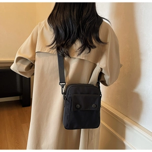 Dettaglio di una borsa a tracolla nera in nylon con tasca a patta su trench beige