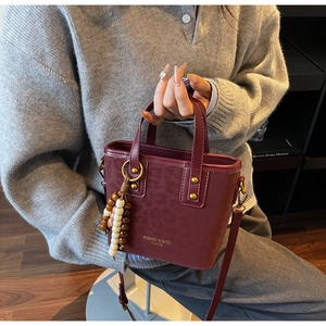 Detail of burgundy leopard print bucket bag with gold lettering and wooden bead charm