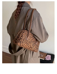 Detail of leopard print baguette bag with brown leather strap worn over a trench coat