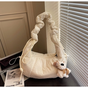 Quilted crescent shoulder bag with dog charm beside a laptop in lifestyle setting