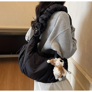 Detail of black quilted shoulder bag featuring wide padded strap and plush puppy charm