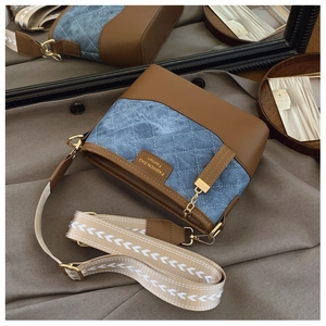 Detail of blue quilted denim bucket bag with brown leather accents and gold hardware