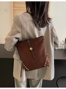 Brown suede bucket bag with gold rivets and adjustable strap shown on model's shoulder