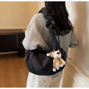 Detail of black puffer shoulder bag featuring a cute white puppy plush keychain charm