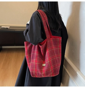 Detail shot of a red plaid canvas tote bag worn on shoulder in a warm lifestyle setting