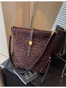 Large leopard print bucket bag with gold studs and shoulder strap on a reflective surface