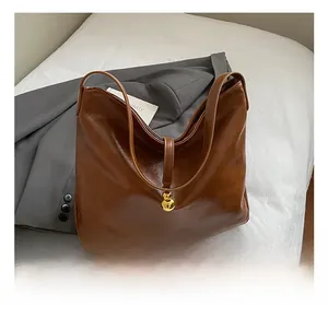 Détail d'un sac cabas en cuir brillant marron avec fermoir boule dorée et logo embossé