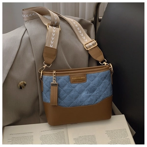 Close-up of quilted denim bucket bag with brown leather trim and wide fabric strap