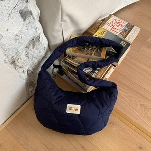Detail of navy quilted moon bag showing heart stitching and pearl logo patch on fabric
