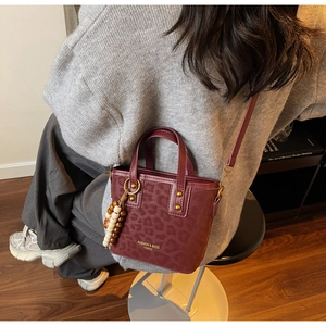 Deep red leopard print crossbody bag with wooden bead charm detail worn by a model