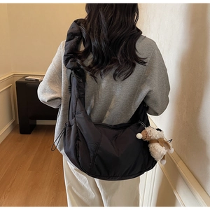 Detail of black crescent crossbody bag with ruched strap and white plush dog charm