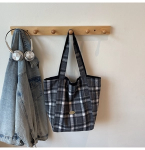 Close-up of checkered canvas tote bag with oval leather patch on a wooden hook