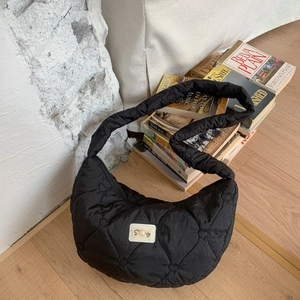 Detail of black heart-quilted puffer bag with pearl logo label on a wooden floor
