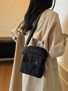 Borsa a tracolla minimalista in nylon nero con tracolla regolabile indossata su un trench