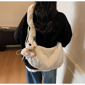 Detail of a beige pleated crossbody bag with a plush bear charm on a female model