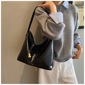 Détail du sac cabas en cuir noir brillant avec pendentif doré et large bandoulière