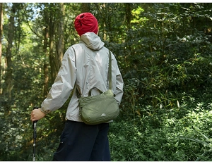 Sac bandoulière outdoor en tissu écossais vert porté par une personne en forêt dense