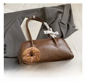 Detail of dark brown leather handbag with donut charm and silk scarf on a grey blazer