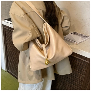 Détail d'un sac cabas minimaliste crème avec breloque boule en métal doré et texture