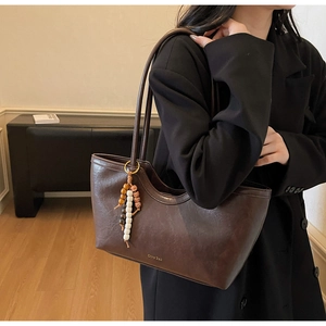 Détail du sac cabas vintage en cuir marron avec pompon en perles de bois et logo de marque