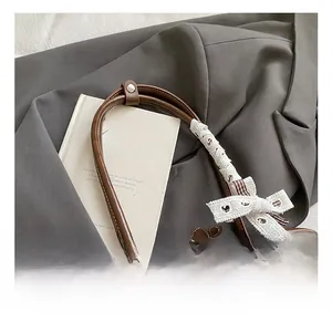 Close-up of brown leather bag handle with white knit bow and silver rivet detail