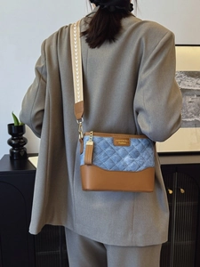 Quilted denim and brown leather bucket bag with wide canvas strap on model in gray suit