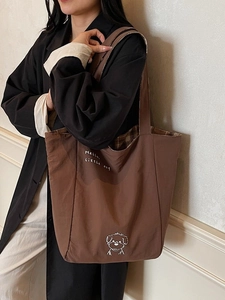 Brown canvas tote bag with embroidered dog and checkered lining worn on shoulder