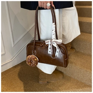 Détail du sac baguette en cuir marron avec nœud en dentelle et breloque beignet en peluche