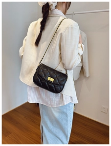 Detail shot of black quilted crossbody bag with gold chain strap worn over a blazer