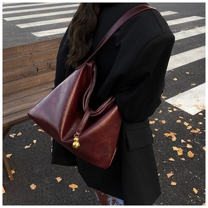 Détail d'un sac cabas vintage rouge foncé avec pendentif doré porté par un mannequin