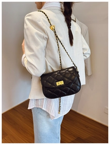 Classic black quilted crossbody bag with gold chain strap shown on person in modern interior