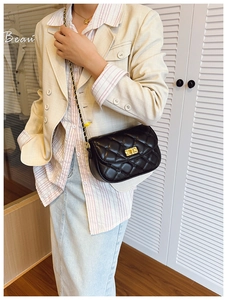 Close-up of black quilted crossbody bag with gold lock on a model in a beige blazer