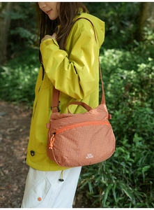 Outdoor view of orange checkerboard crossbody bag with logo and adjustable strap
