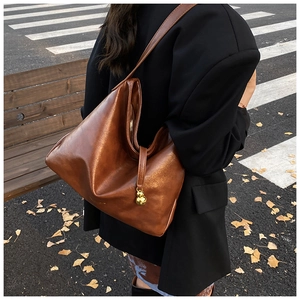 Détail d'un grand sac cabas en cuir marron avec un pendentif gourde dorée et une fermeture