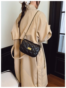Quilted black chain crossbody bag worn by a model in a stylish trench coat