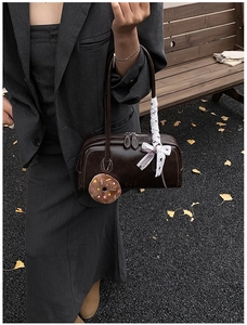 Détail du sac bowling en cuir marron foncé avec charm donut et ruban blanc élégant