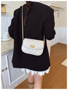 Close-up of quilted cream crossbody bag with gold chain strap worn by model in black suit