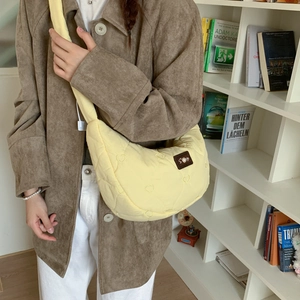 Detail of light yellow heart-quilted dumpling bag with pearl leather tag and wide strap
