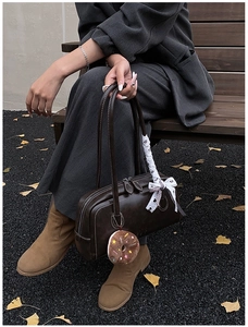 Detail of dark brown retro shoulder bag with plush donut charm on a wooden bench