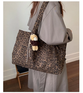 Detail of leopard print tote bag featuring a cute brown bear charm and wide shoulder strap