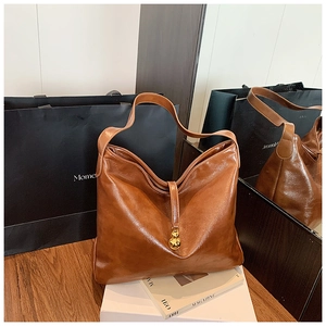 Détail d'un grand sac hobo en cuir huilé marron avec un pendentif sphérique doré chic