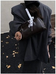 Sac baguette vintage marron avec nœud en dentelle et breloque peluche sur un banc