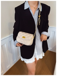 Close-up of beige quilted crossbody bag featuring gold chain strap and metal lock detail