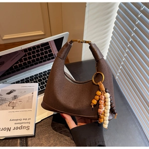 Détail d'un sac hobo en cuir marron avec pompon en perles de bois et poignée métallique