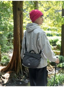 Detail of a black checkered nylon crossbody bag with zipper, carried by a hiker in the woods