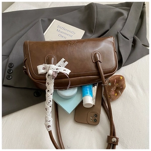 Détail du sac cylindrique marron en cuir ciré avec ruban en dentelle blanche à cœurs