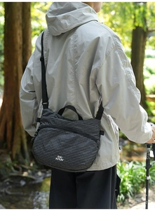 Détail d'un sac bandoulière noir à texture quadrillée avec une poignée de transport